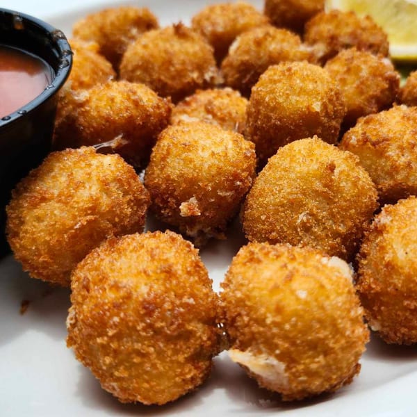 A plate of golden-brown fried boudin balls with a side of dipping sauce and a lemon wedge.