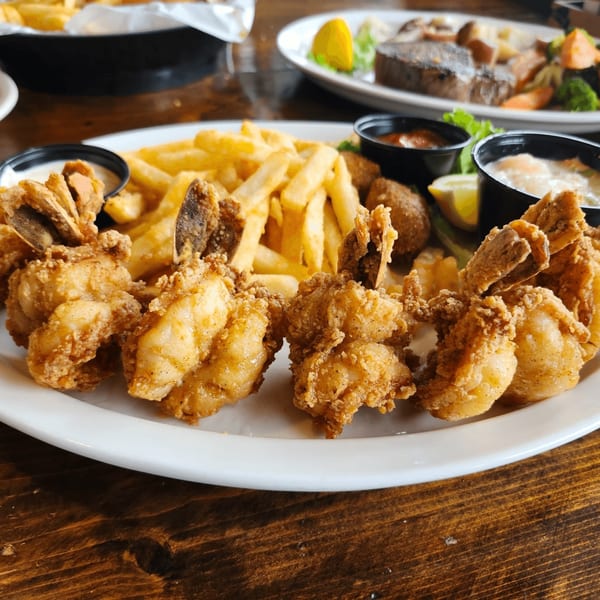 A plate of Crazy Alan's Swamp Shack fried shrimp, french fries, and hush puppies with dipping sauces.