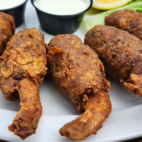 Close-up of crispy fried alligator tails with dipping sauces and a lemon wedge on a white plate.
