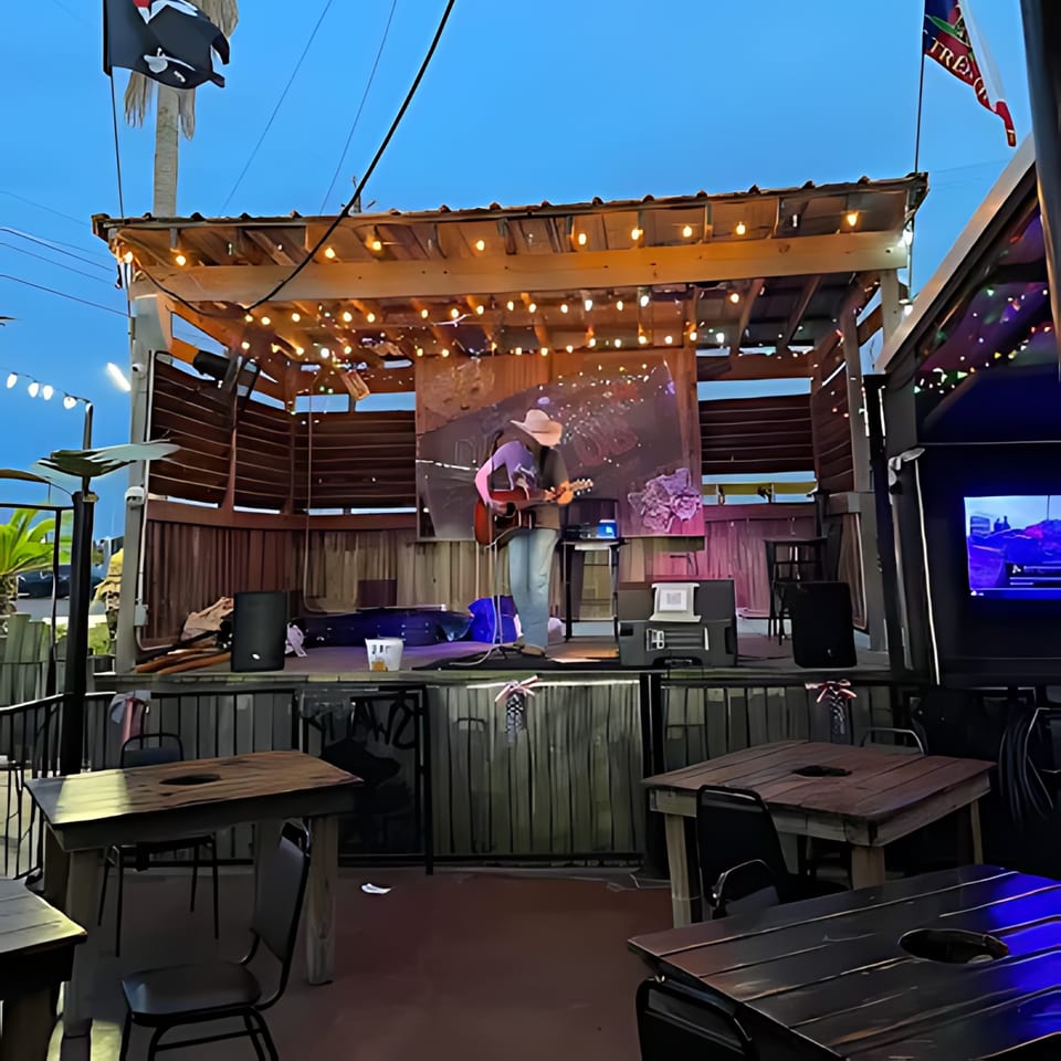 A musician plays guitar on an outdoor stage at Crazy Alan's Swamp Shack, with empty tables in the foreground.