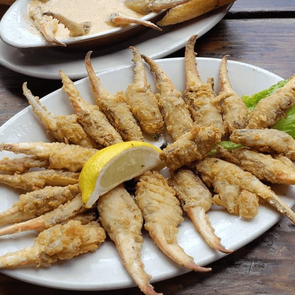 A plate of golden-fried alligator tail pieces with a lemon wedge and lettuce, with a bowl of dipping sauce in the background.