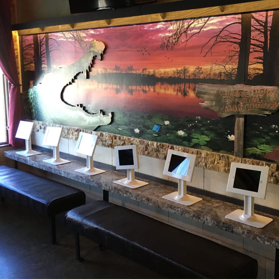 A wall mural of a swamp at sunset with a large alligator cutout and tablets on a counter.