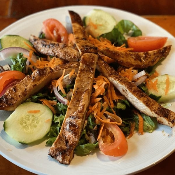Grilled chicken salad with lettuce, tomatoes, cucumbers, carrots, and red onions on a white plate.