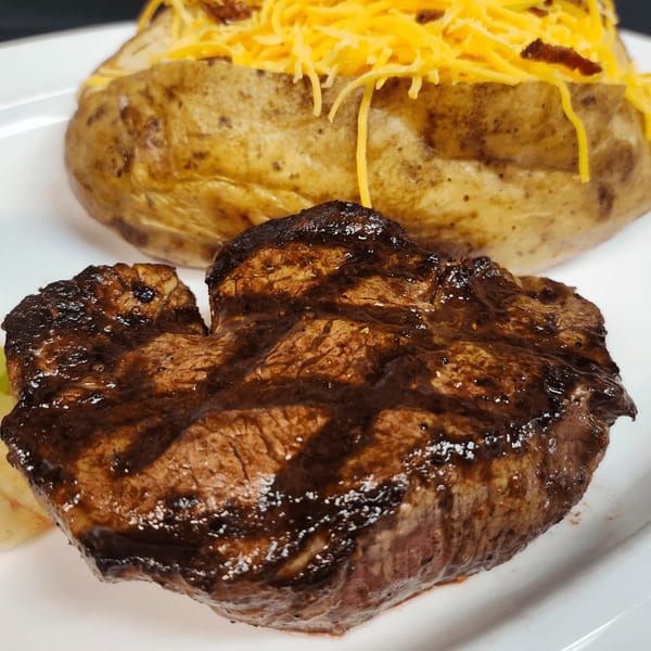 Grilled steak with grill marks and a baked potato topped with shredded cheese and bacon bits.