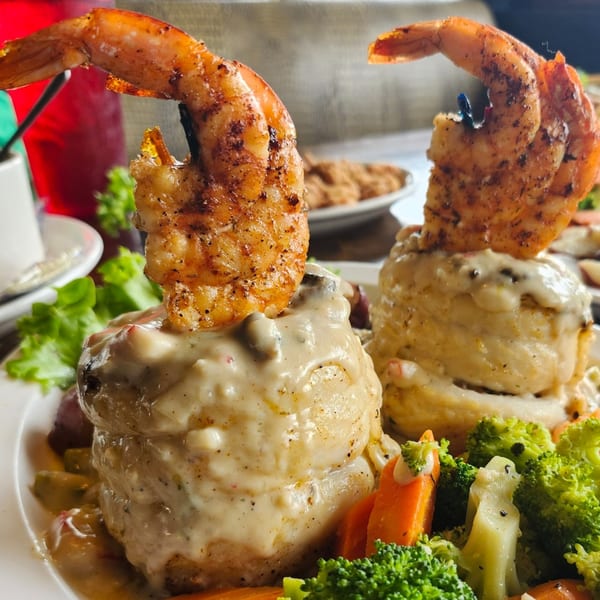 Two Cajun shrimp and grits dishes, topped with creamy sauce and served with broccoli and carrots.