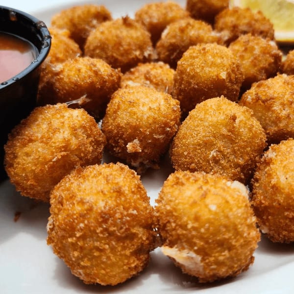 Golden-brown fried boudin balls with a side of dipping sauce and a lemon wedge.